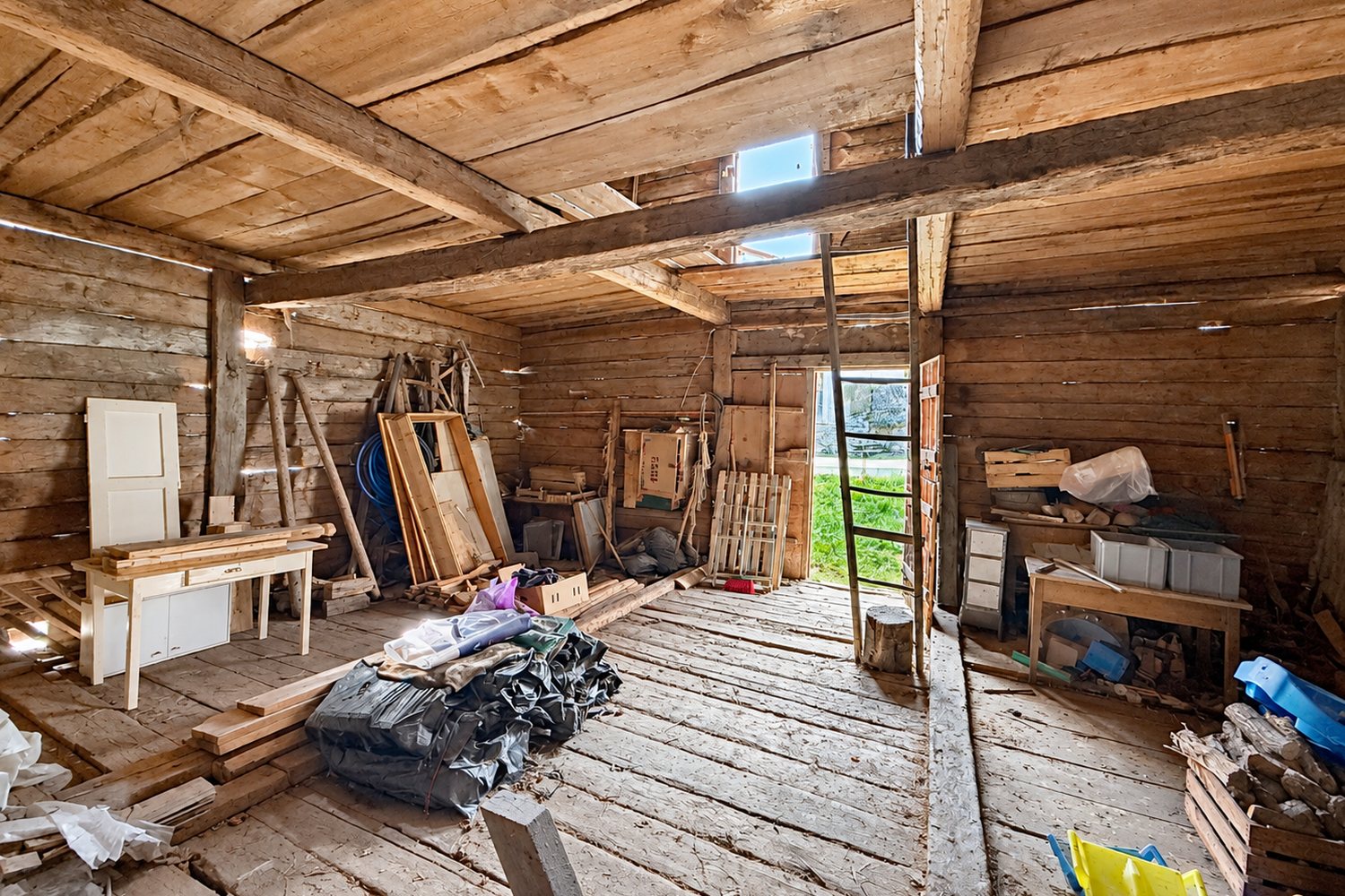 L'intérieur du niveau de grange, plancher large, porte ouverte sur la verdure du hameau.