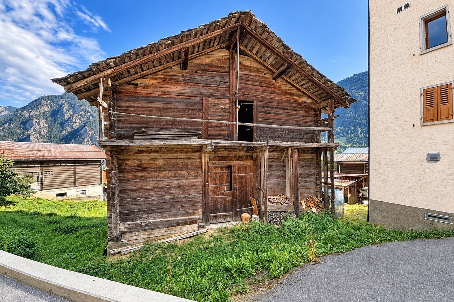 La façade est de la grange avec sa porte haute, entre les maisons du hameau, montagnes au loin.